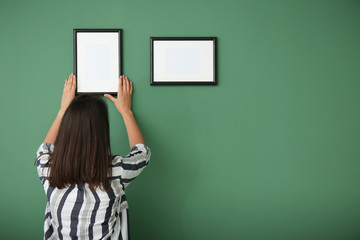 Woman hanging picture frame on color wall