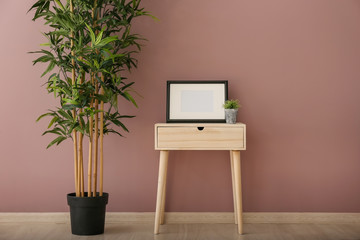 Wooden table with frame and green plant near color wall