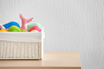 Wicker basket with balls of knitting yarn and funny toy on table against light background