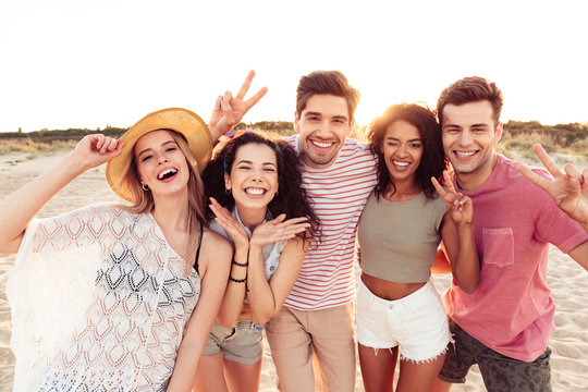 Portrait of happy young multiracial girls and guys 20s in summer clothes taking selfie, while resting at seaside