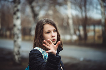 Schoolgirl with backpack walks in depressed state along city street in cloudy weather in rain....