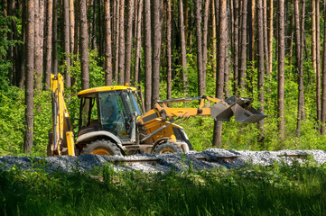 Yellow excavator pours gravel on the construction of the railway in the forest © Oksana