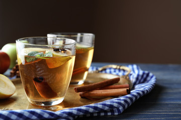 Tray with glass of apple drink and cinnamon on table
