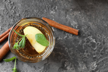 Tasty drink with cinnamon and apple slices in glass on grey textured background