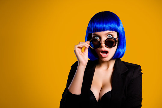 Portrait with copyspace empty place of afraid scared girl looking out glasses with big eyes wide open mouth in bright blue wig isolated on yellow background