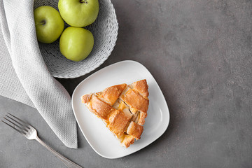 Plate with piece of delicious pie and apples on grey background, top view