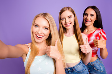 Self portrait of successful friendly girls shooting selfie on front camera gesturing thumb up sign with finger isolated on vivid violet background. Rest relax leisure concept