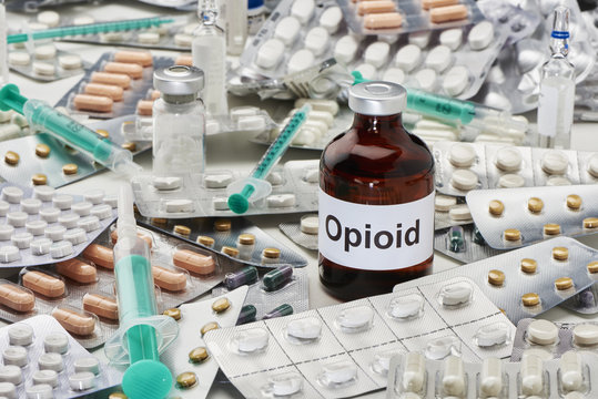 Eine Ampulle Opioid welche umgeben ist von Tabletten Verpackungen und Spritzen sowie anderen Ampullen