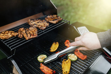 Young man grilling some meat and vegetable on huge grill.