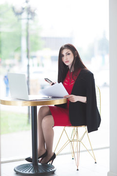 handsome young lady in trendy dress with documents and phone at table laptop