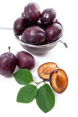 Steel colander with ripe plums, whole and half ripe plums with leaf isolated on a white background..