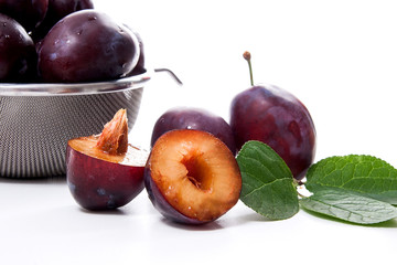 Steel colander with ripe plums, whole and half ripe plums with leaf isolated on a white background..