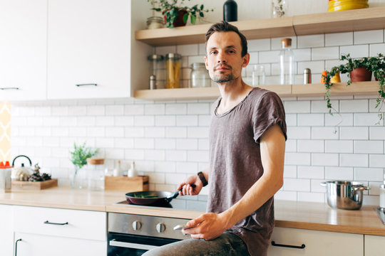 Portrait of brunet man with frying pan in his hands talking on phone in kitchen