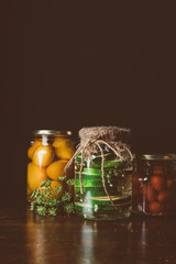glass jars with preserved vegetables on wooden table in dark kitchen