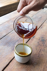 Coffee drip in coffee pot pouring into the ceramic cup on the wooden table in coffee shop