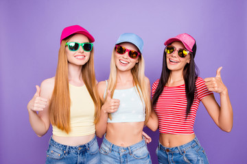 Portrait of cheerful positive trio with beaming smiles gesturing thumb up signs isolated on bright...