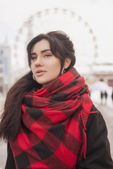 Cute young caucasian brunette woman student on a walk in europe city streets. She wearing blac coat and plaid red scarf. Cold winter weather