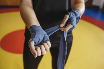 Woman bandage her hands before box sparring on a ring in gym. Close up of her hands