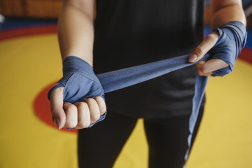 Woman bandage her hands before box sparring on a ring in gym. Close up of her hands