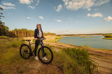 Fototapeta na wymiar The beautiful girl is standing by bicycle. Senior woman riding a bike beside a lake. A female biker take a rest after biking