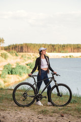 Obraz premium The beautiful girl is standing by bicycle. Senior woman riding a bike beside a lake. A female biker take a rest after biking