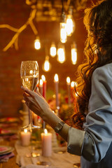 Woman standing neat wedding table, celebrate with a glass of wine in her hand. No face. Decor, candles and edison lamps on a background