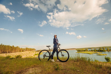 The beautiful girl is standing by bicycle. Senior woman riding a bike beside a lake. A female biker take a rest after biking