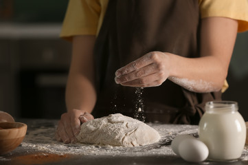 Obraz na płótnie Canvas Woman sprinkling dough with flour on kitchen table