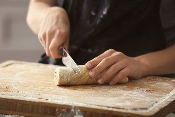 Woman cutting dough for cinnamon rolls on wooden board