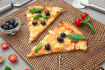 Slices of tasty Italian pizza with olives on wicker mat