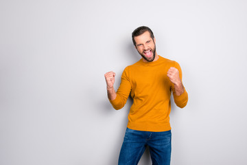 Portrait of handsome successful  man dressed in yellow sweater dark blue jeans celebrating his victory isolated on gray background copy-space