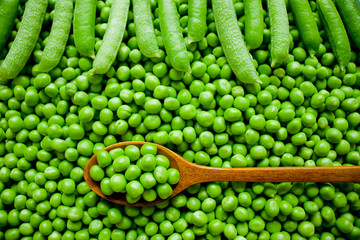 Fresh peas in wooden spoon on green peas.