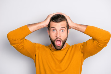 Close up portrait of shocked frustrated with open mouth holding head with hands with big eyes wearing bright yellow sweater isolated on gray background