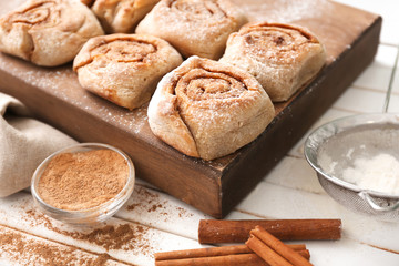 Naklejka premium Board with delicious cinnamon buns on wooden background