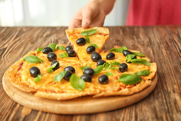 Woman taking slice of tasty pizza with olives from wooden table