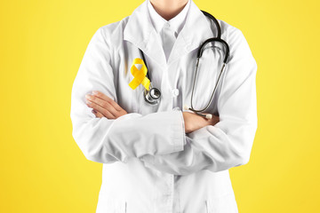 Doctor with yellow ribbon on robe against color background. Cancer awareness concept