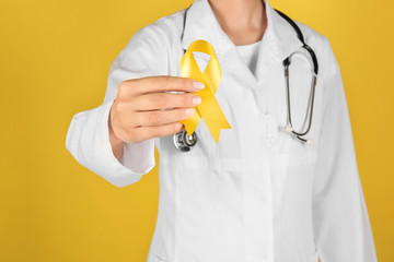 Doctor with yellow ribbon on color background. Cancer awareness concept