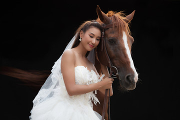 Young beautiful beauty bride in fashion white wedding costume stand with handsome horse on black background