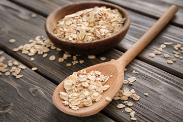 Bowl and spoon with raw oatmeal on wooden background