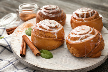 Wooden board with tasty cinnamon buns on table