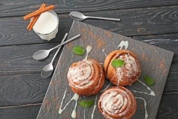 Slate plate with tasty cinnamon buns and glass of milk on wooden table