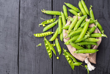 A pods of peas in a bag on black wooden background