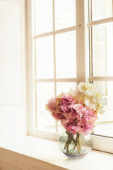Glorious pastel pink bouquet in glass jug on windowsill by window. Flowers in interior design. Cozy home.
