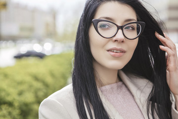 Woman with long black hair on a walk in city park. She wears a classic (or smart casual) coat in cold windy weather. Copy space