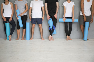 Fototapeta na wymiar Group of sporty people with yoga mats near grey wall