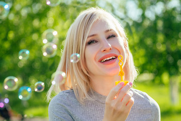 attractive blond woman blowing soap bubbles in the park on a background of green grass . bubble and...