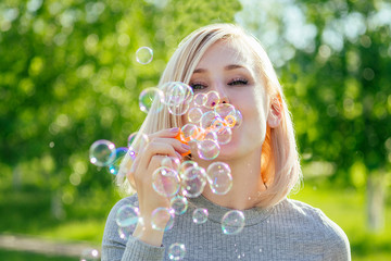 attractive blonde girl blowing soap bubbles in the park on a background of green grass . bubble and holiday atmosphere