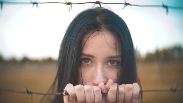 girl brunette refugee behind barbed wire camp slow lifestyle motion video. the concept of freedom is upset Woman hands and barbed wire. girl Refugee, prison, refugees captivity concept