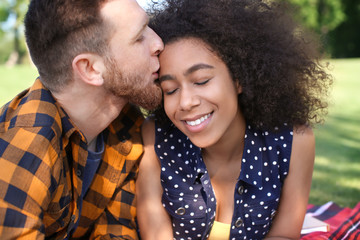 Fototapeta premium Young loving interracial couple resting in park on spring day