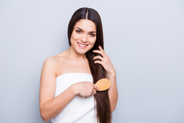 Portrait of pretty brunette woman with long strong hair combing with brush wrapped in white towel isolated on grey background. Dry ends oiled damage minerals haircut therapy effect concept
